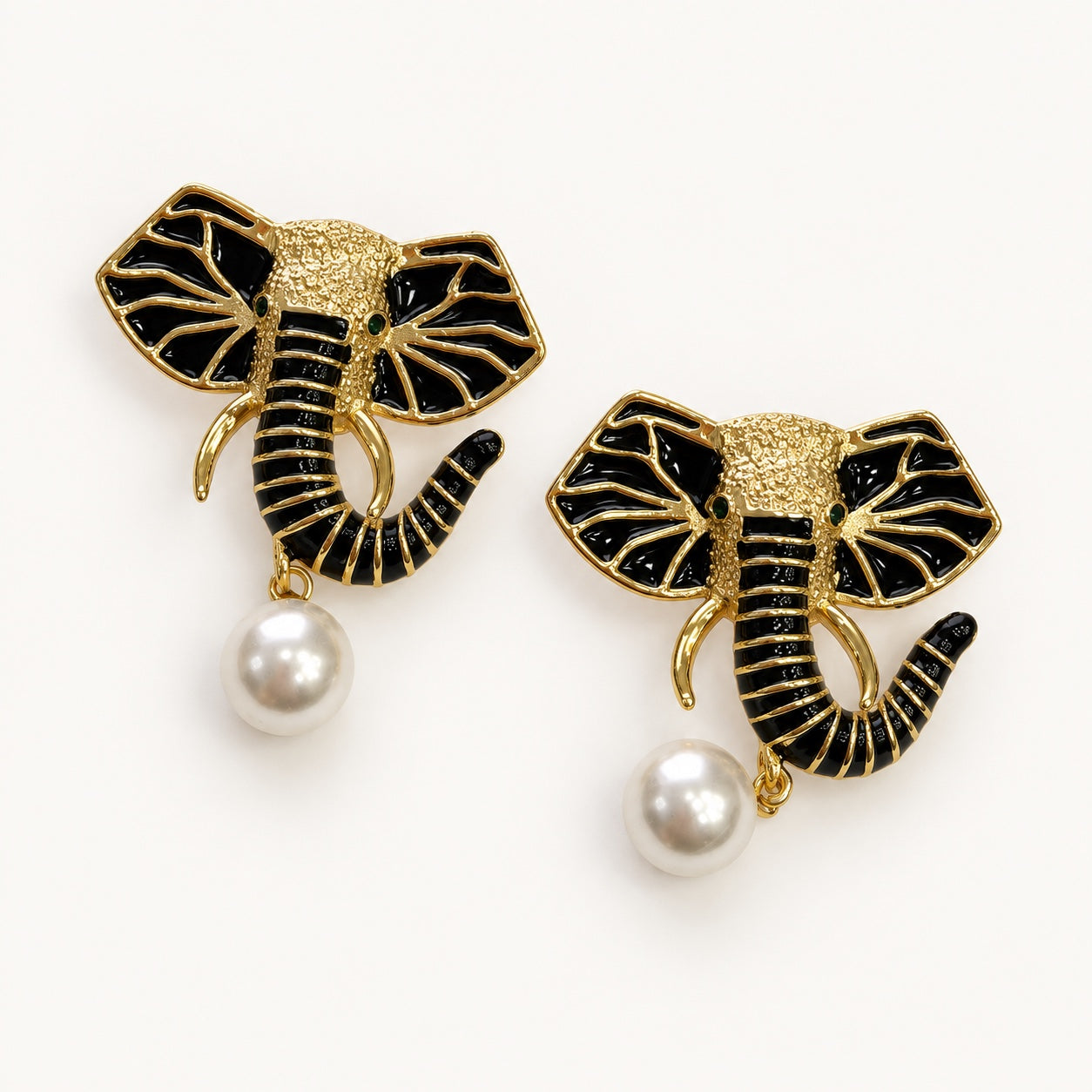 Coppia di orecchini PHILO P a elefante nero e color oro con occhi verdi e pendente bianco dall’effetto perlato.