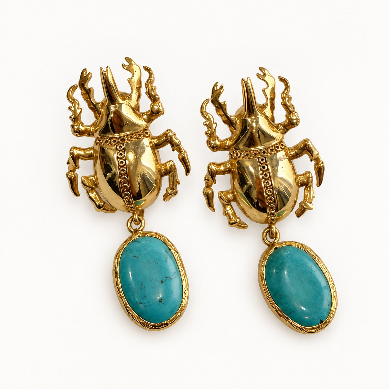 Coppia di orecchini con motivo scarabeo color oro e pendenti ovali color turchese su fondo chiaro.
