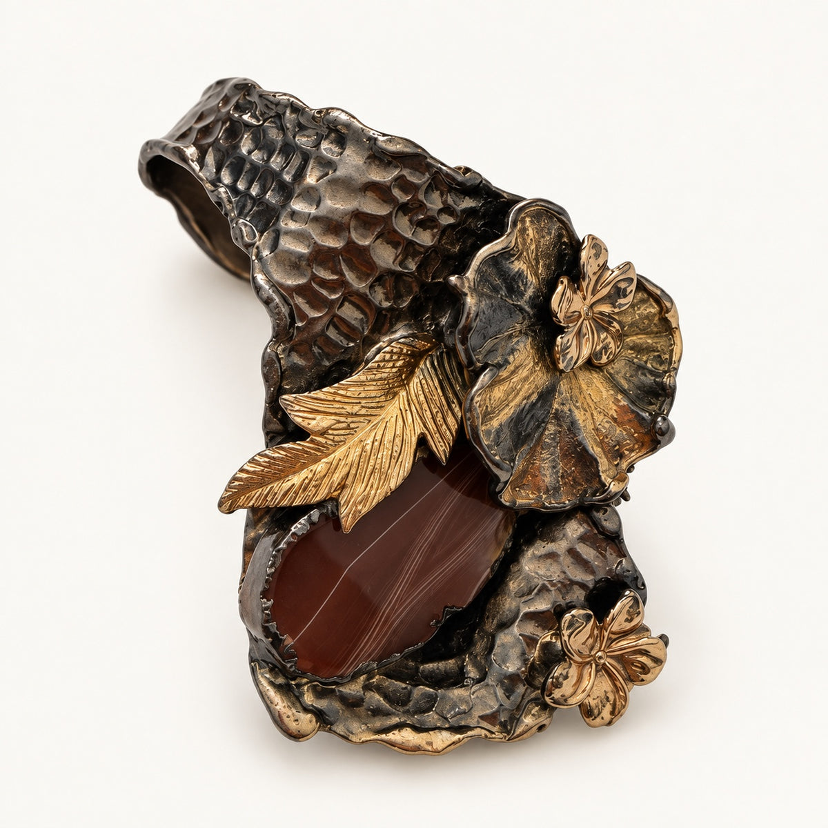 Anello con fiore e foglia visto a tre quarti, con dettaglio marrone venato e fascia martellata.