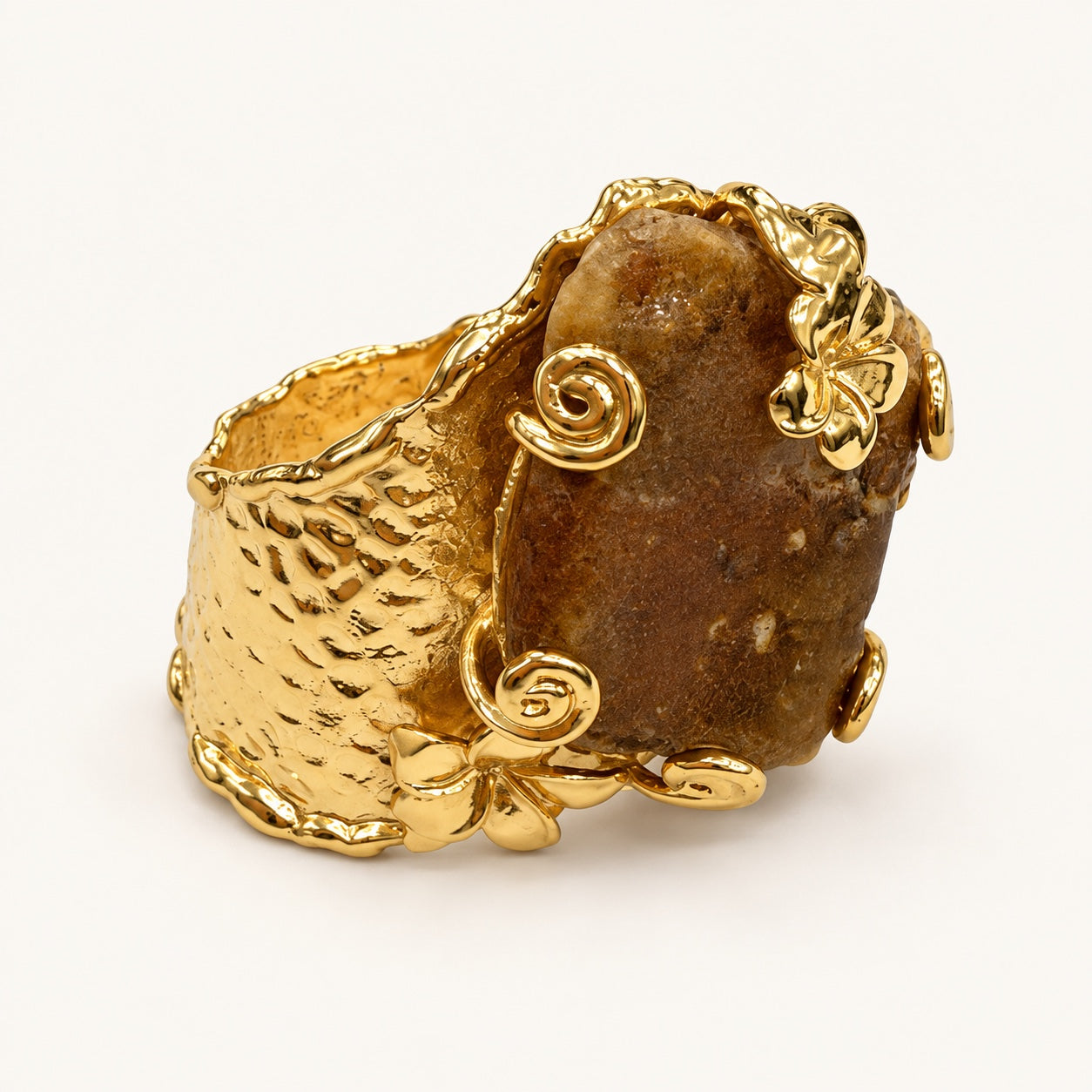 Anello color oro e marrone visto a tre quarti, con superficie martellata, fiori e spirali in rilievo.