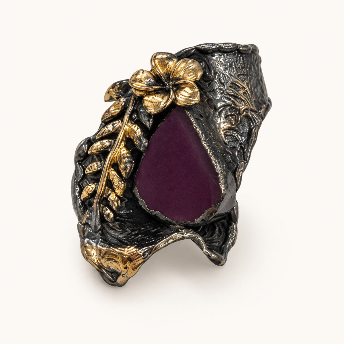 Anello floreale viola visto a tre quarti, con fiore e foglie in rilievo e accenti color oro.