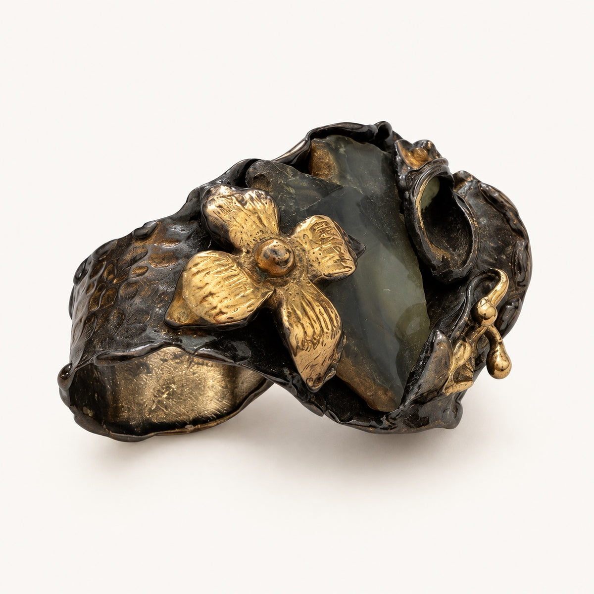 Profilo dell'anello con fiore color oro, dettaglio verde scuro inclinato e fascia curva color canna di fucile.