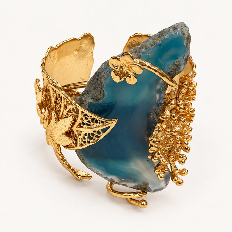 Bracciale aperto PHILO P color oro con elemento centrale blu irregolare e decorazioni botaniche, vista frontale.